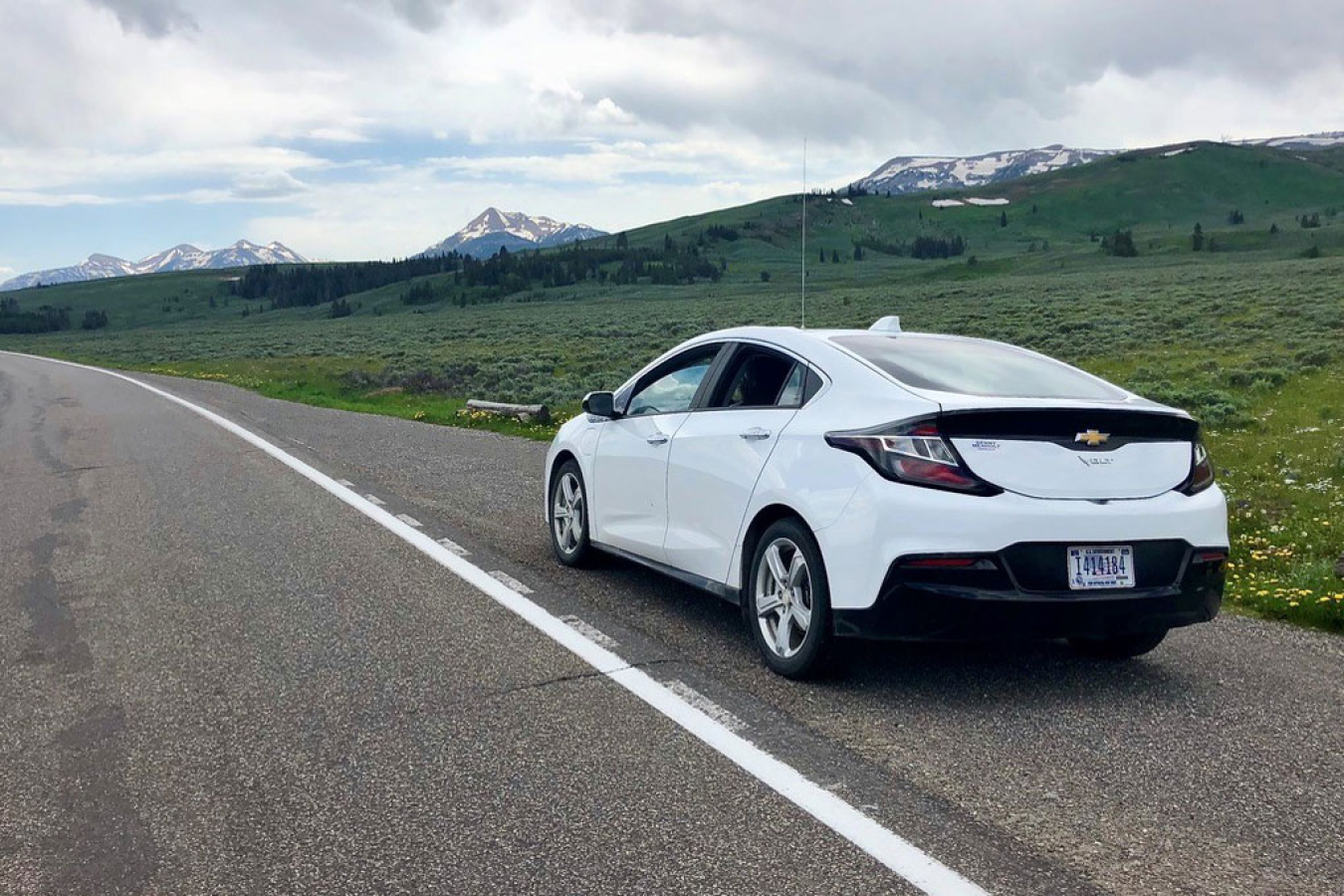 An electric vehicle parked on the side of a road with a large open field in the background and mountains.