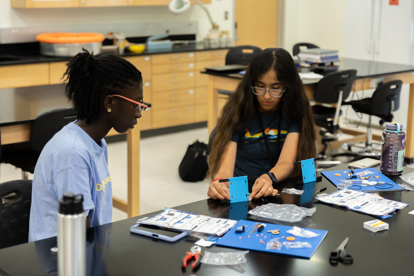 Two girls sit at a table and put together pieces of a science project.