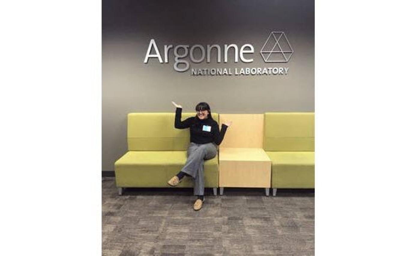 Brenda Escobedo sitting on sofa in front of the Argonne National Laboratory sign.