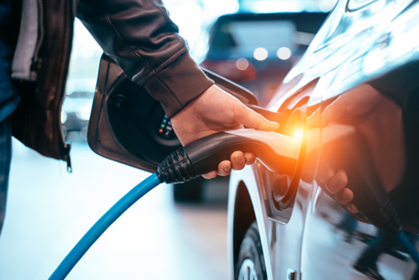 Human hand charges their vehicle at an EV charging station. 