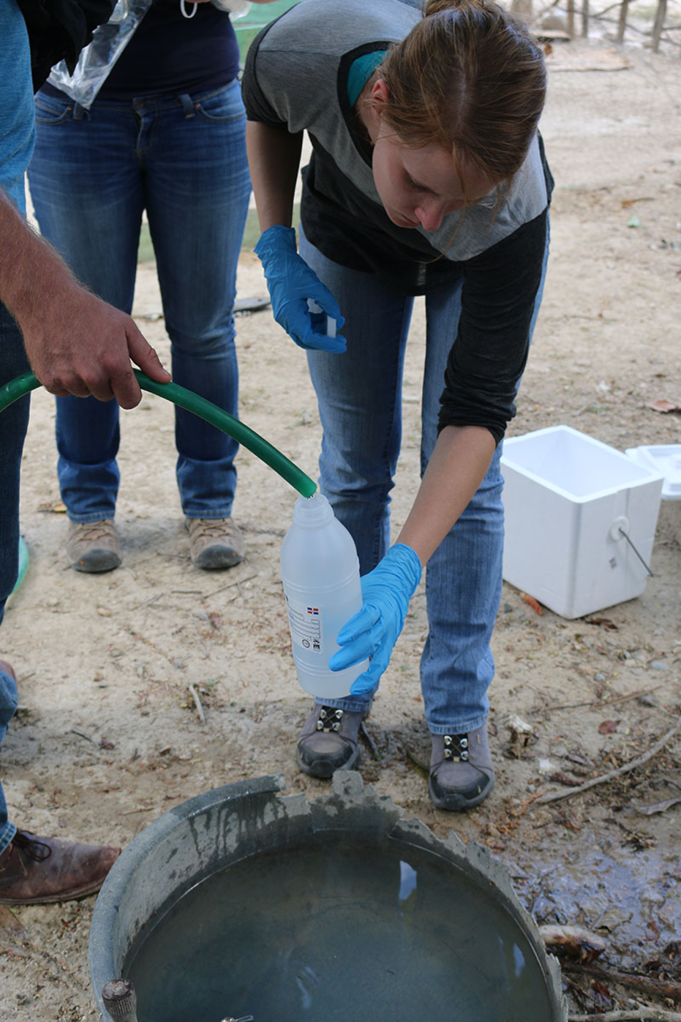 Sarah Moore leans forward to fill a plastic water bottle with water from a hose.