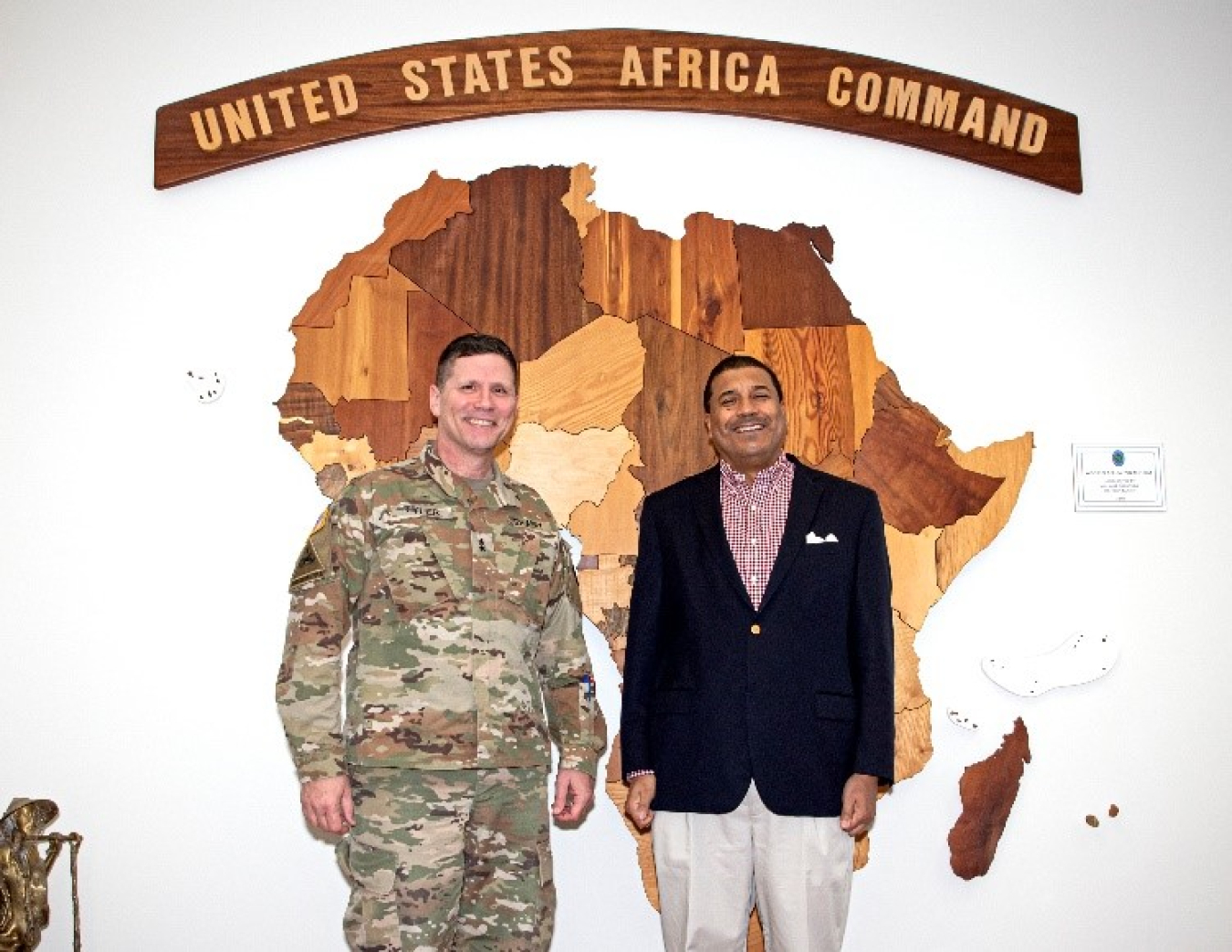 Rose and Tyler stand in front of a large map of Africa made of wood. The word United States Africa Command are above it.