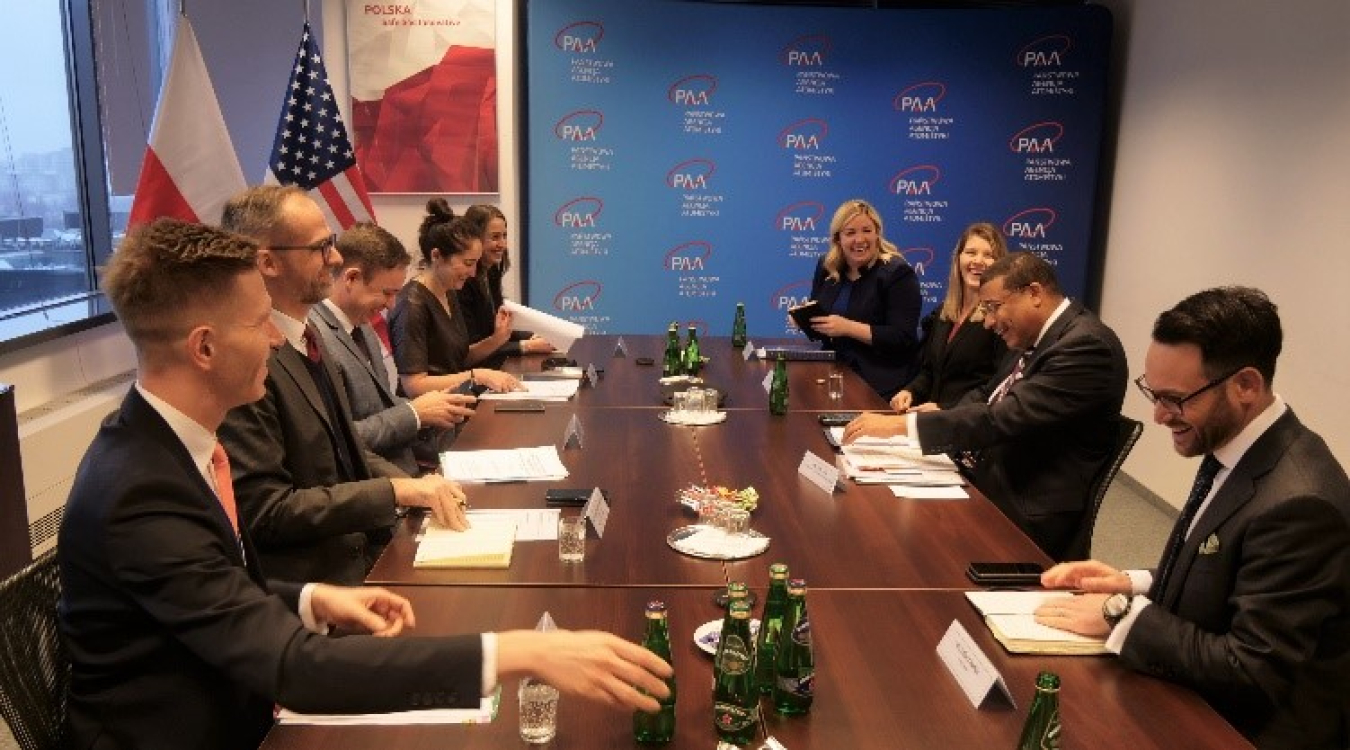 Frank Rose at a long table. There are American and Polish flags in the background.