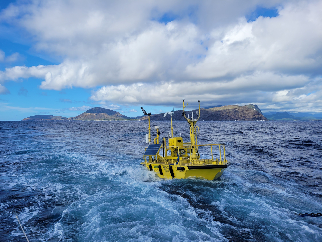 A buoy with lots of instruments floats in the ocean with an island in the background.