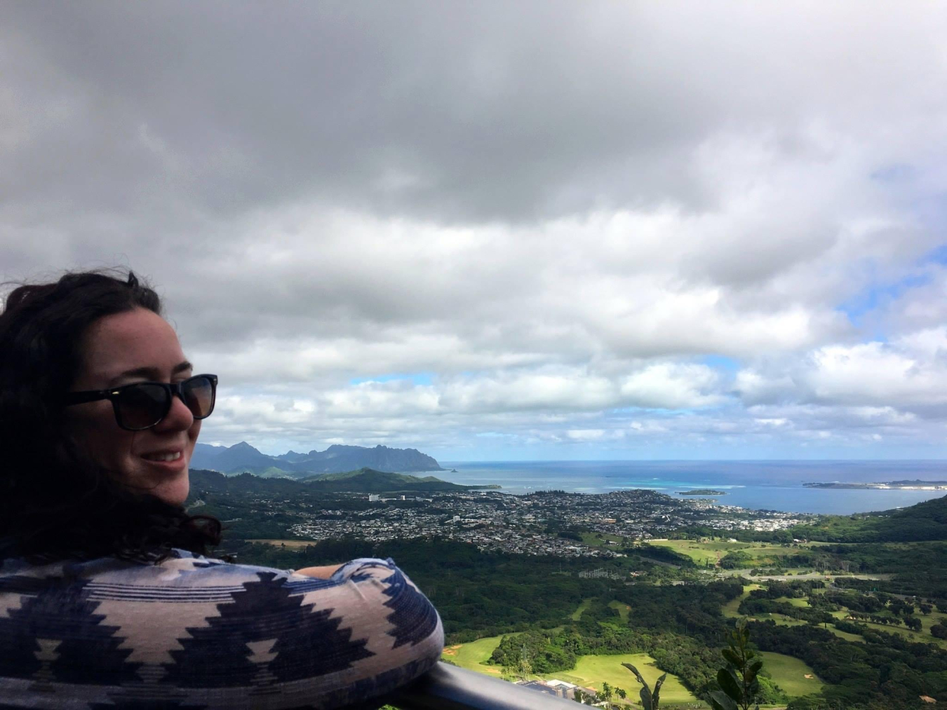Nina Joffe sits on top of a mountain, looking out over fields, forest, and an ocean cove