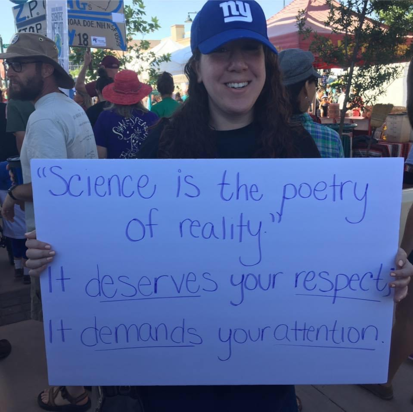Nina Joffe standing in a crowd, holding a sign that reads: "Science is the poetry of reality. It deserves your respect; it demands your attention."