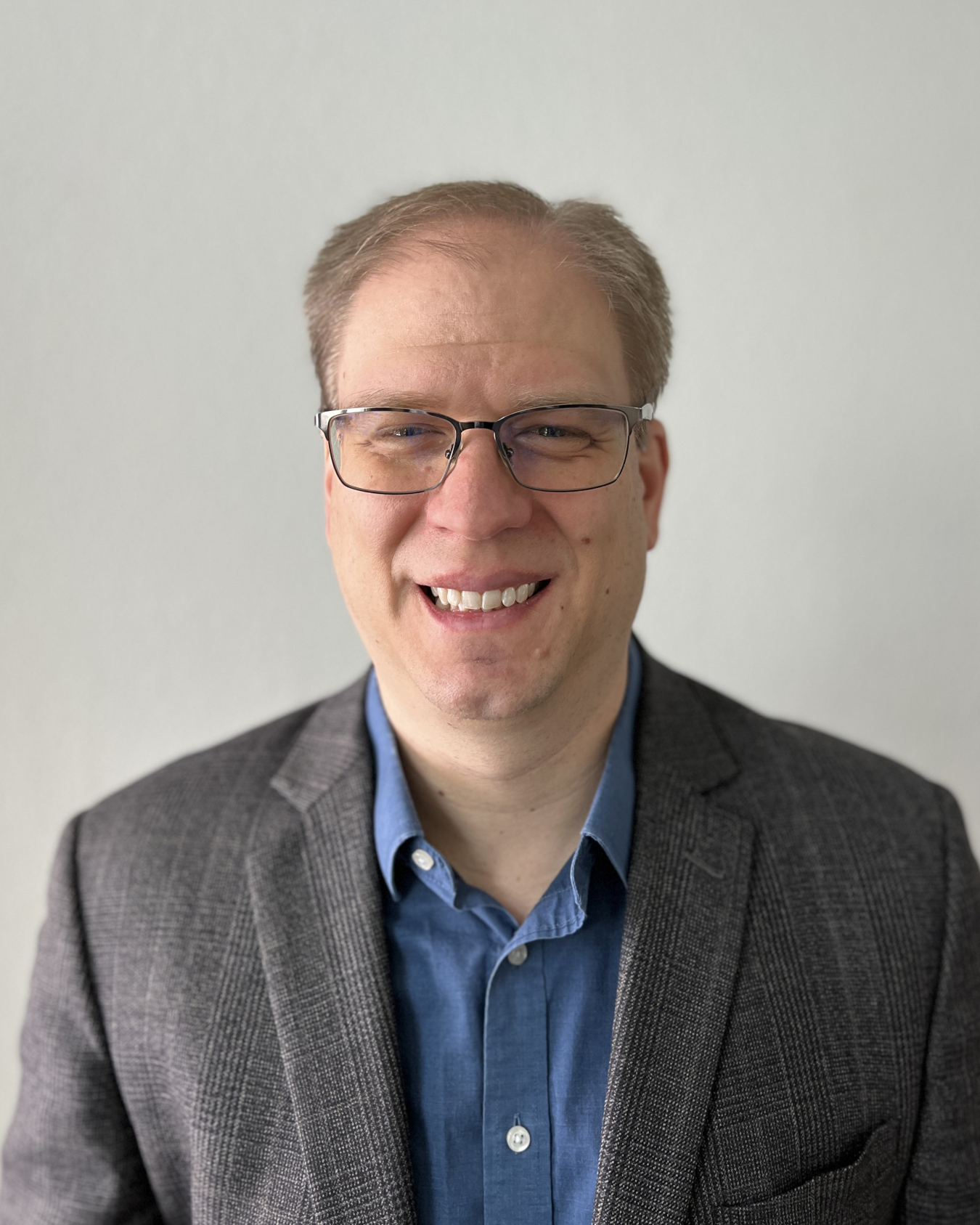 A man in a suit and glasses smiles for the camera.