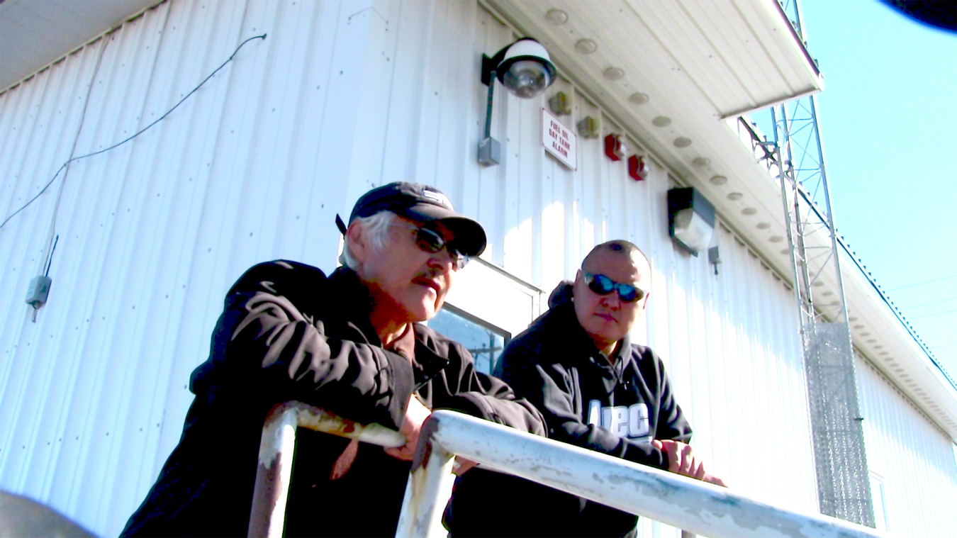 Two men chat outside a utility building. 