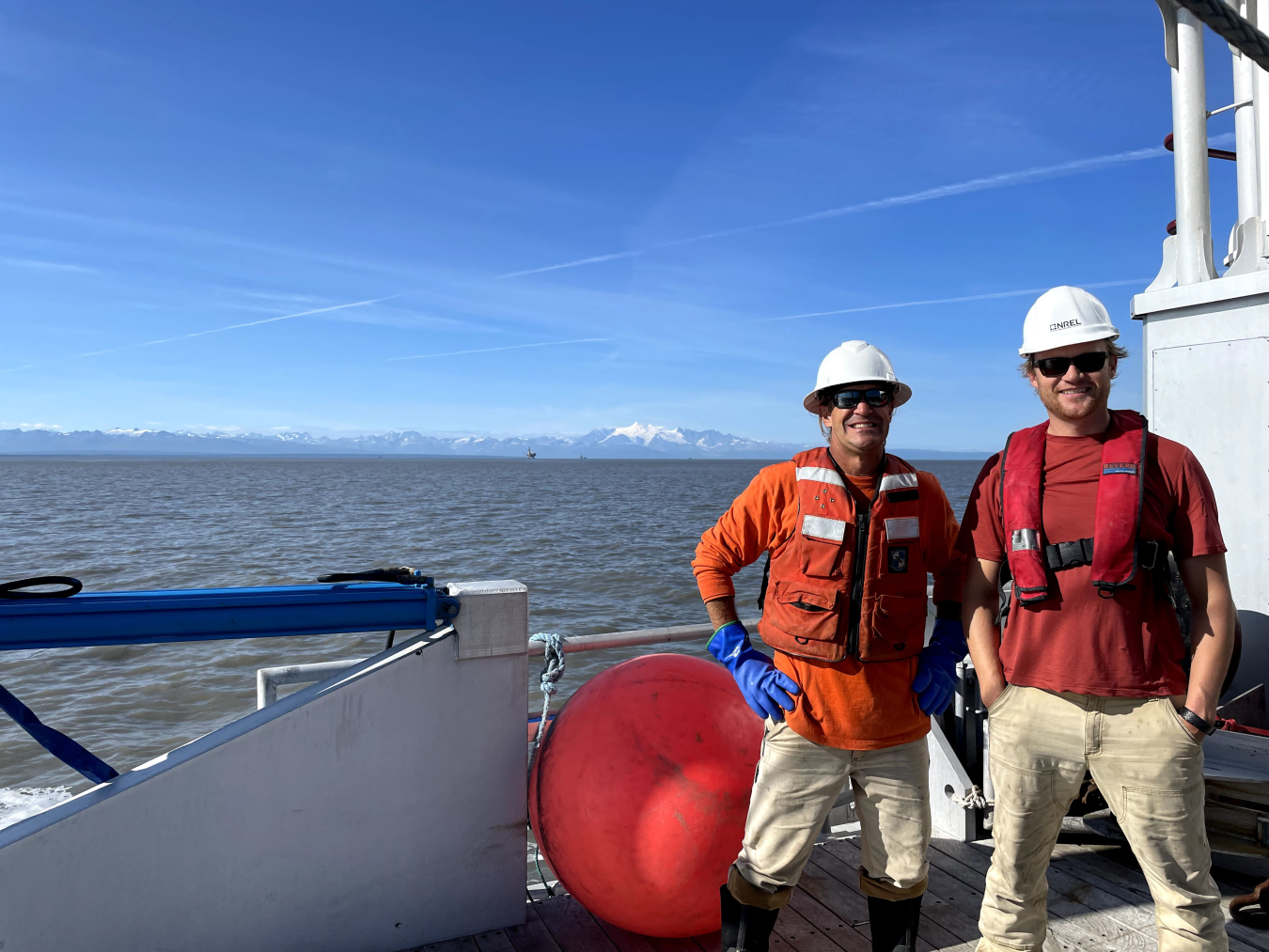 Two men in hard hats standing on the deck of a boat.