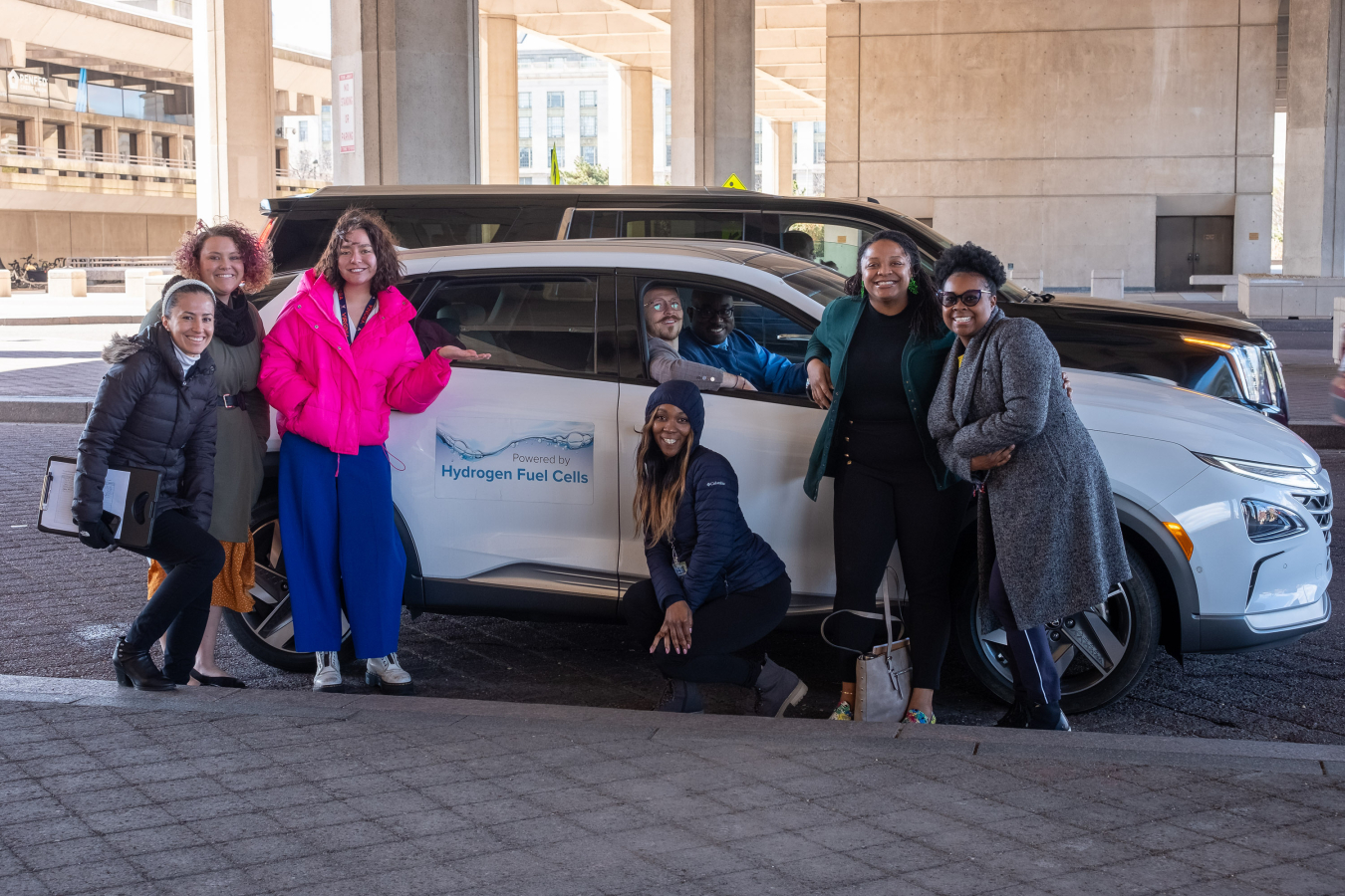 A group of women stand around a white hydrogen fuel cell car.