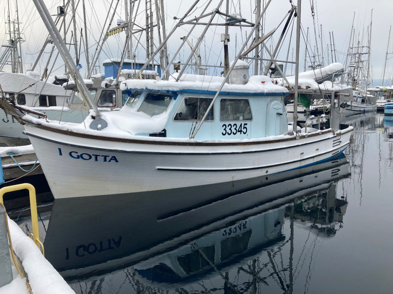 A fishing boat at dock with snow on it, with other boats around it.