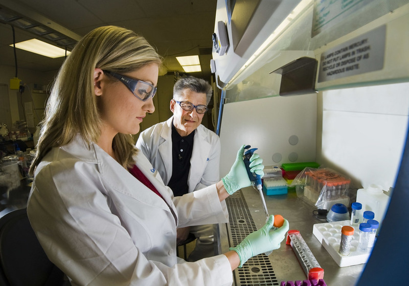 a man and women wearing lab coats and goggles, working in a lab.