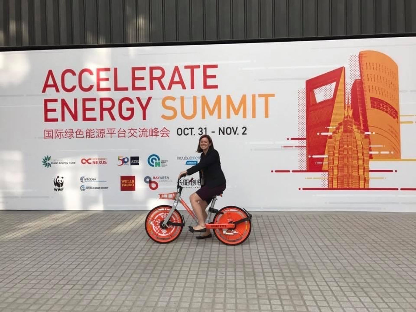 A person riding a bicycle in front of a sign that reads Accelerate Energy Summit