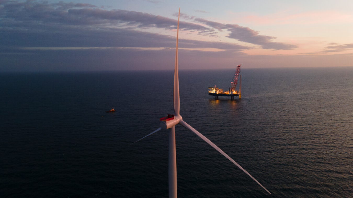 A view from behind an ocean-bound wind turbine with an installation boat and smaller safety boat in the horizon.