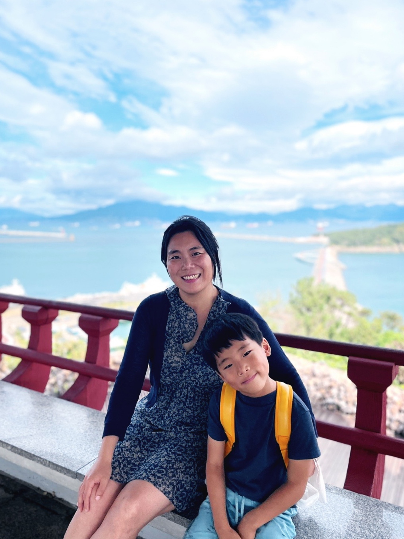 woman and child sitting near ledge overlooking body of water