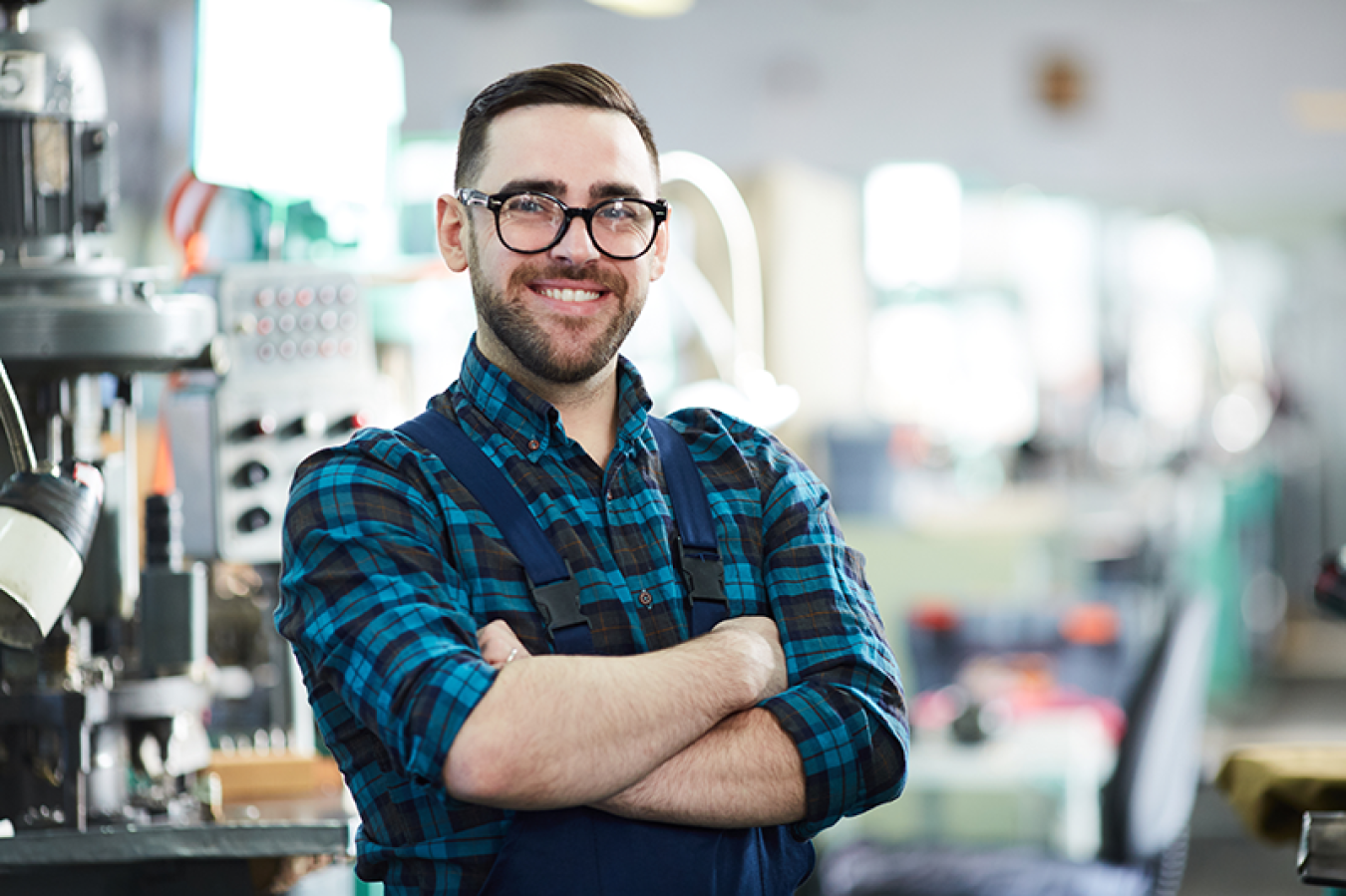 Waist up portrait of cheerful factory worker looking at camera while posing in workshop standing with arms crossed