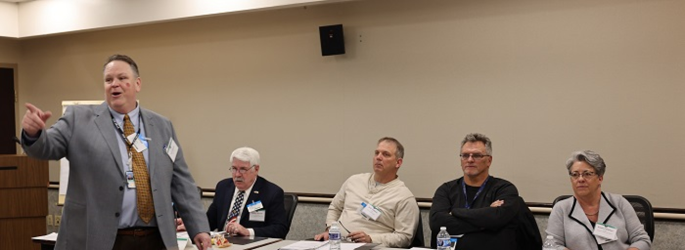 At far left, Eric Roberts, facilitator, speaks during the EM Site-Specific Advisory Board (SSAB) National Chairs meeting. In the background, from left, are Robert Skinner, Idaho SSAB vice chair; Jody Crabtree, Portsmouth SSAB chair; Herman Potter, Portsmouth SSAB vice chair; and Susan Coleman, Hanford SSAB chair.