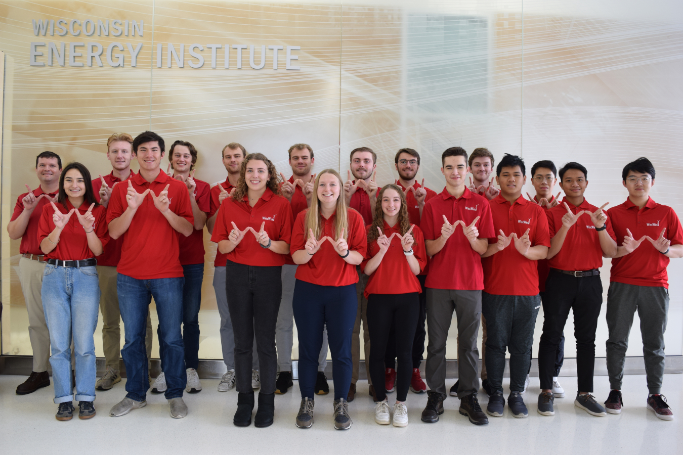 Two rows of students in matching red shirts holding their thumbs and pointer fingers in the shape of a W.