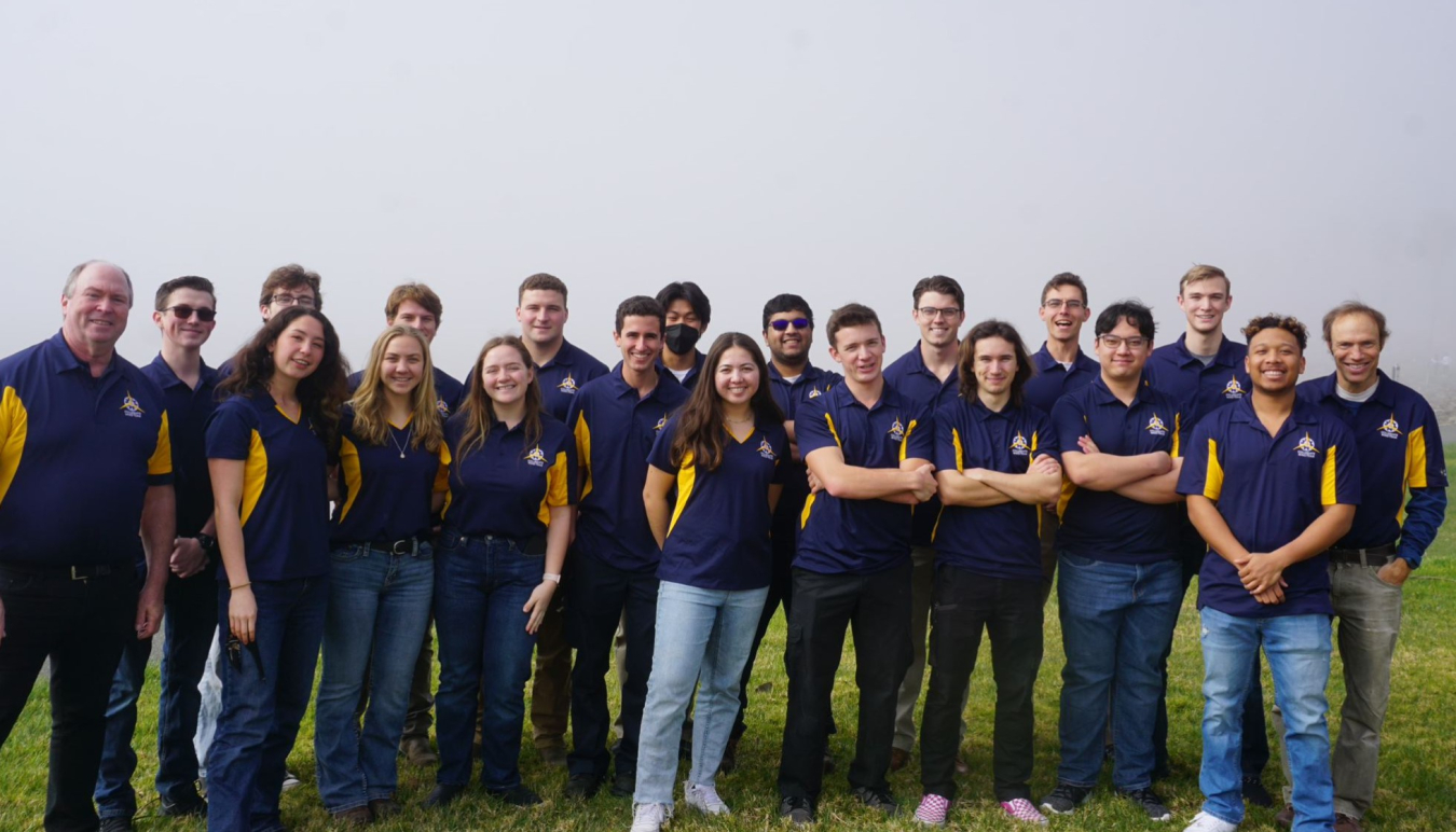 Two rows of students in matching shirts standing in a grassy area.