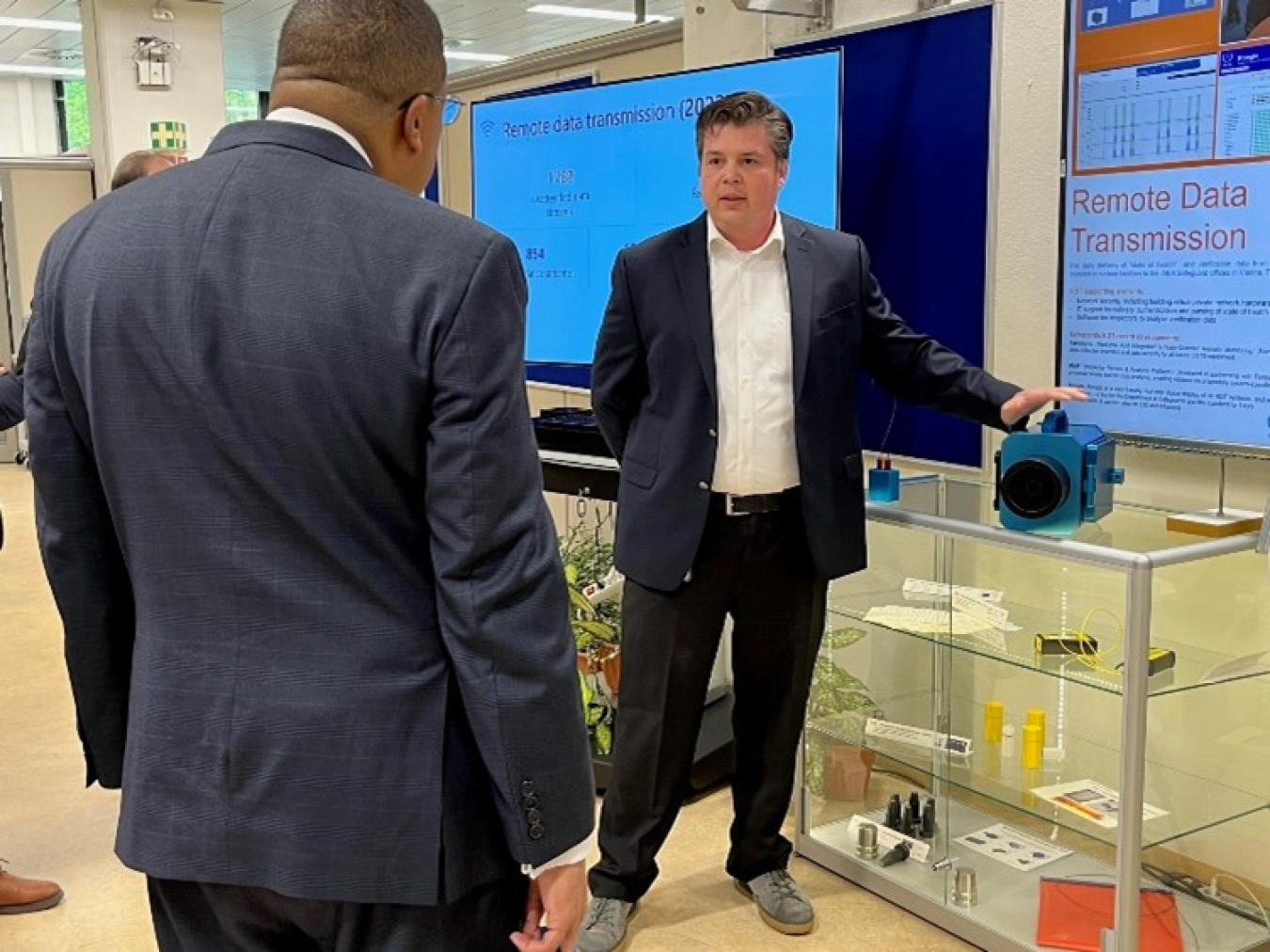A man describes detection equipment to Frank Rose, who has his back to the camera.