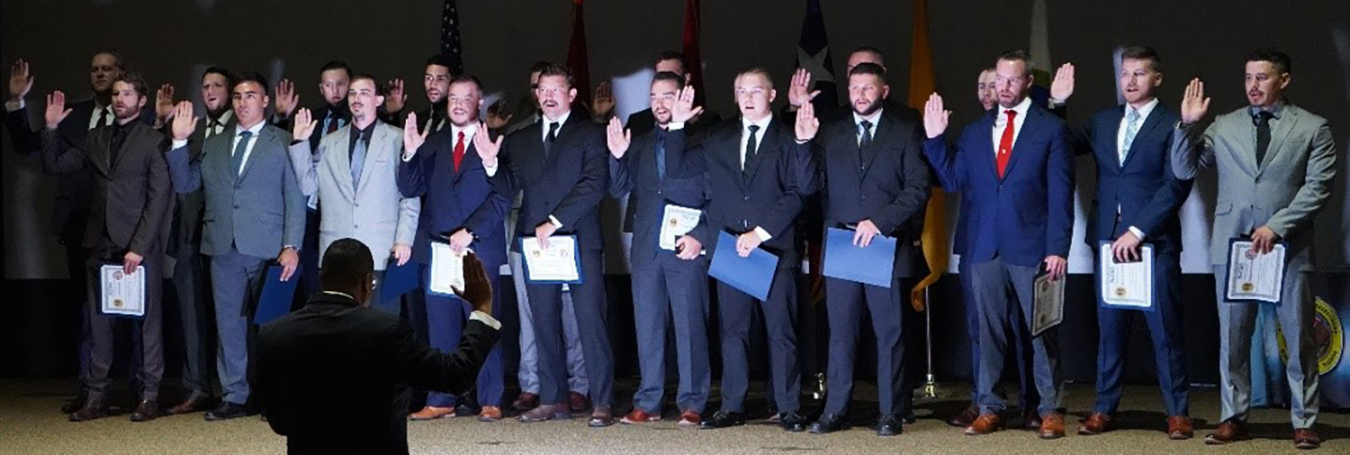 Frank Rose swears in 20 Office of Secure Transportation Agents. They are on stage and he is looking up at them. Everyone's hands are raised in an oath.
