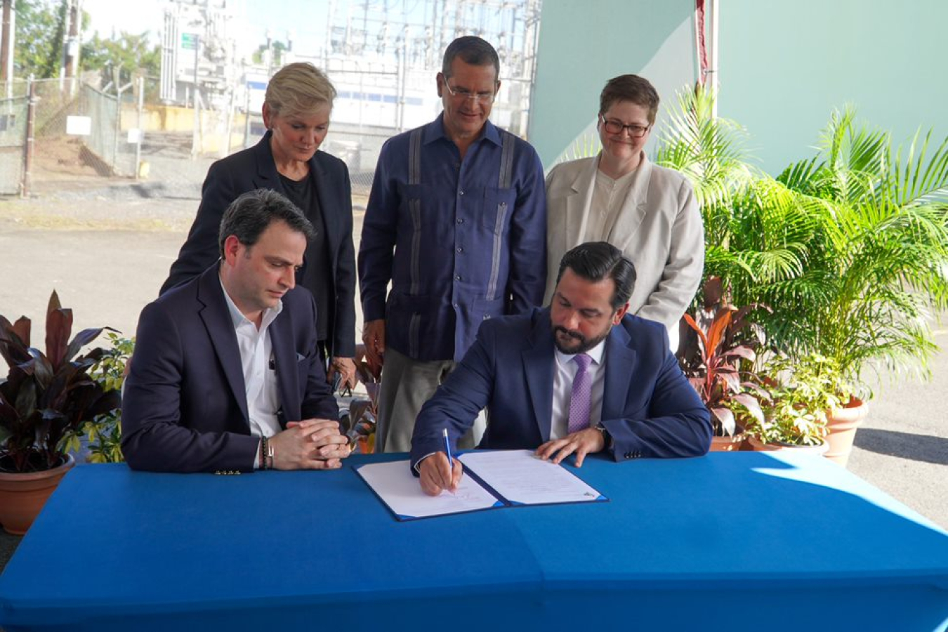 A group of people gathered around a table witnessing the signing of an official document.