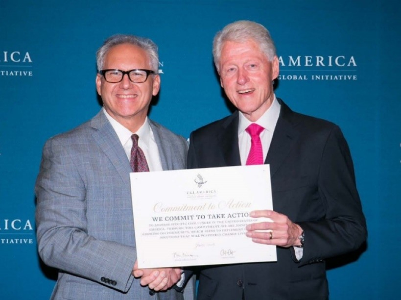 Mark Glick shaking hands with former President Bill Clinton, who is holding up an award certificate.