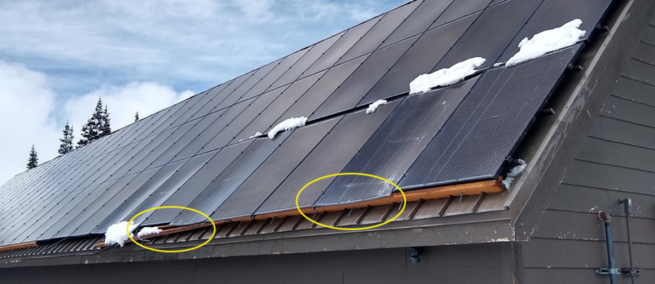 Damaged rooftop solar panels with some snow cover.