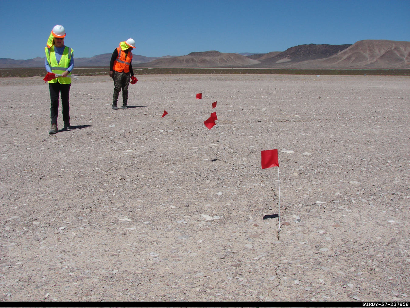 EM Nevada Program Real-time Radiography Technician Byron Smith, right, marks a subsidence crack with flags at the Nevada National Security Sites. Subsidence cracks can form in the earth’s surface over time.