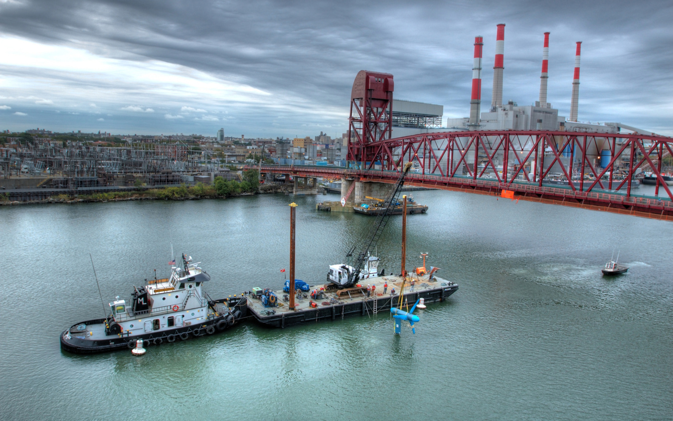 A barge on a river lowering a tidal turbine into the water.