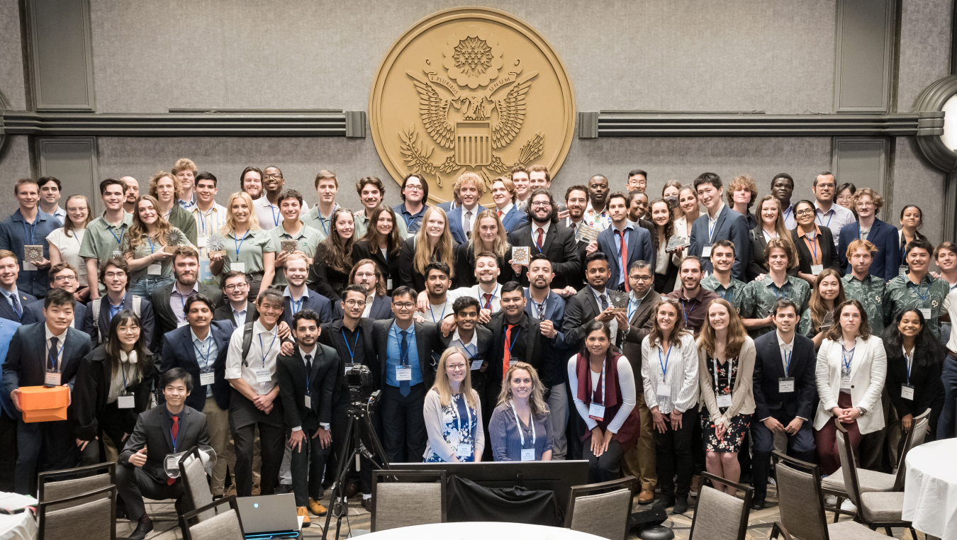 A group of people in business attire and name tags in front of the U.S. seal.