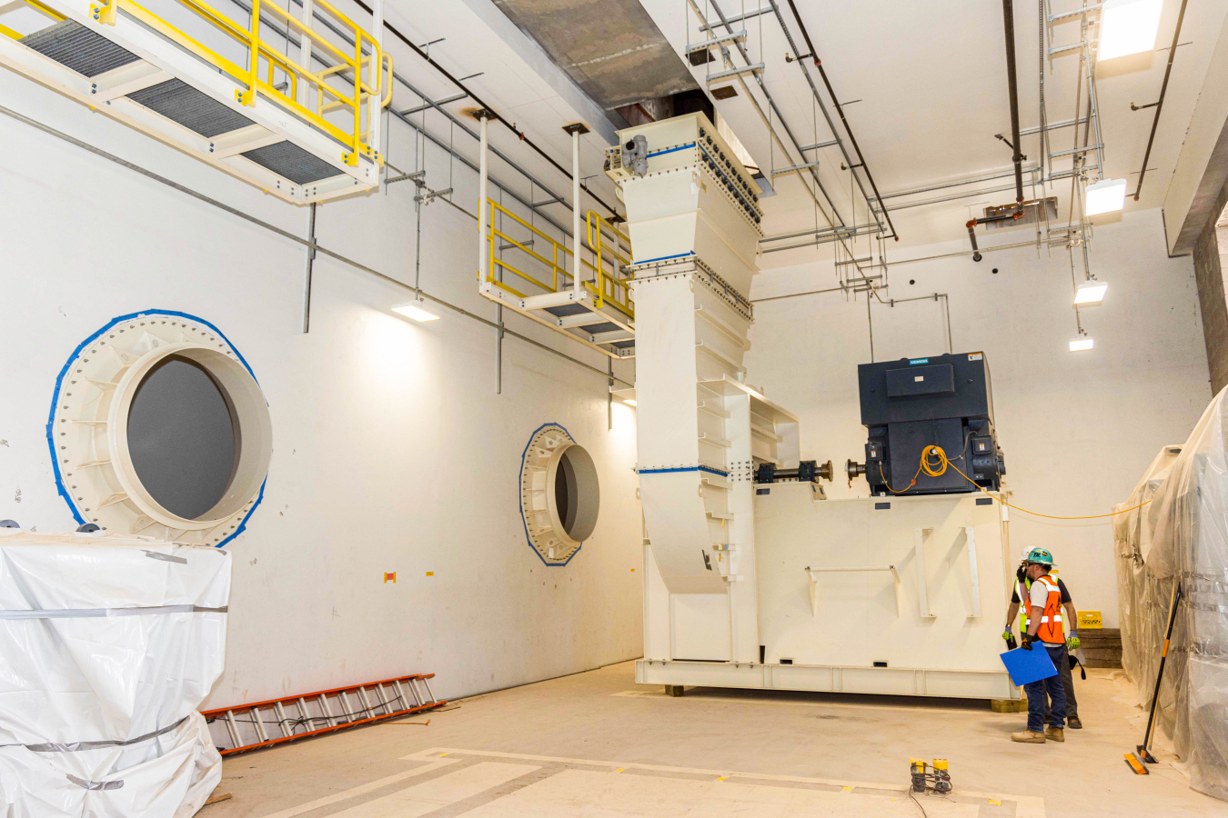 As part of the Safety Significant Confinement Ventilation System, 20-foot-tall exhaust fan assemblies are being placed in the New Filter Building for eventual hookup to the ports at left that come from HEPA filter banks. The 1,000-horsepower motors will pull 540,000 cubic feet per minute of air through the system, compared to the 170,000 cubic feet per minute of filtered air through the current system. Air will be exhausted upward and then out through a 125-foot-tall stack.