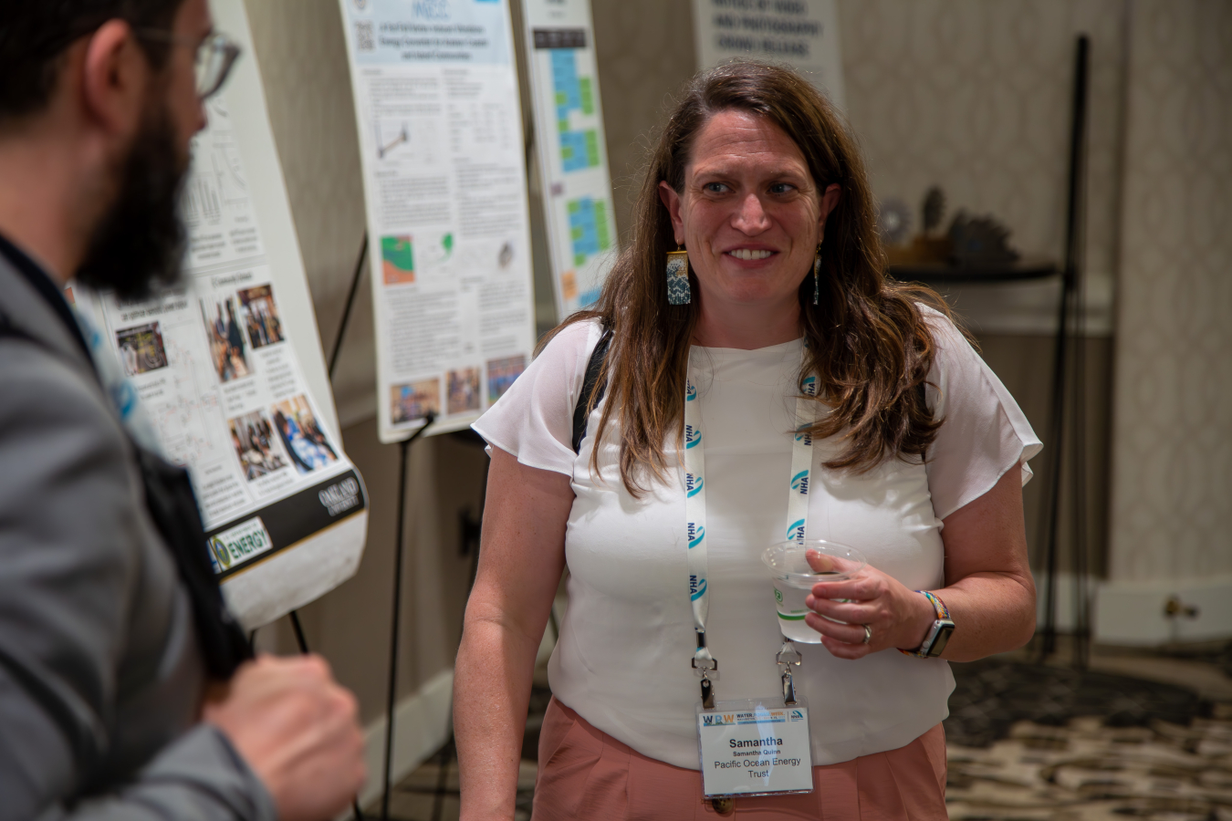Samantha Quinn laughing with another person in front of a poster of an island.