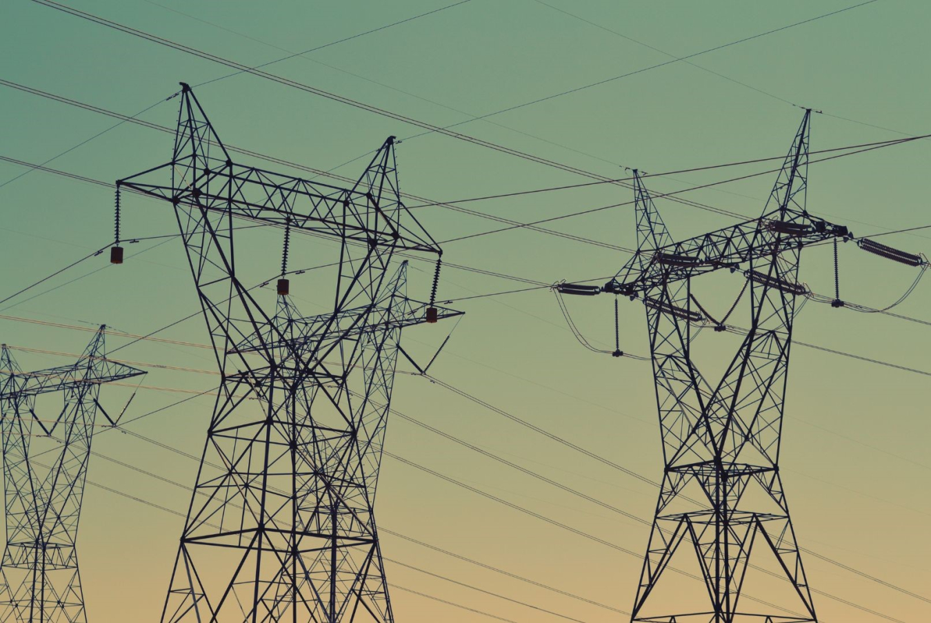 Transmission towers and power lines against a faded sunset sky