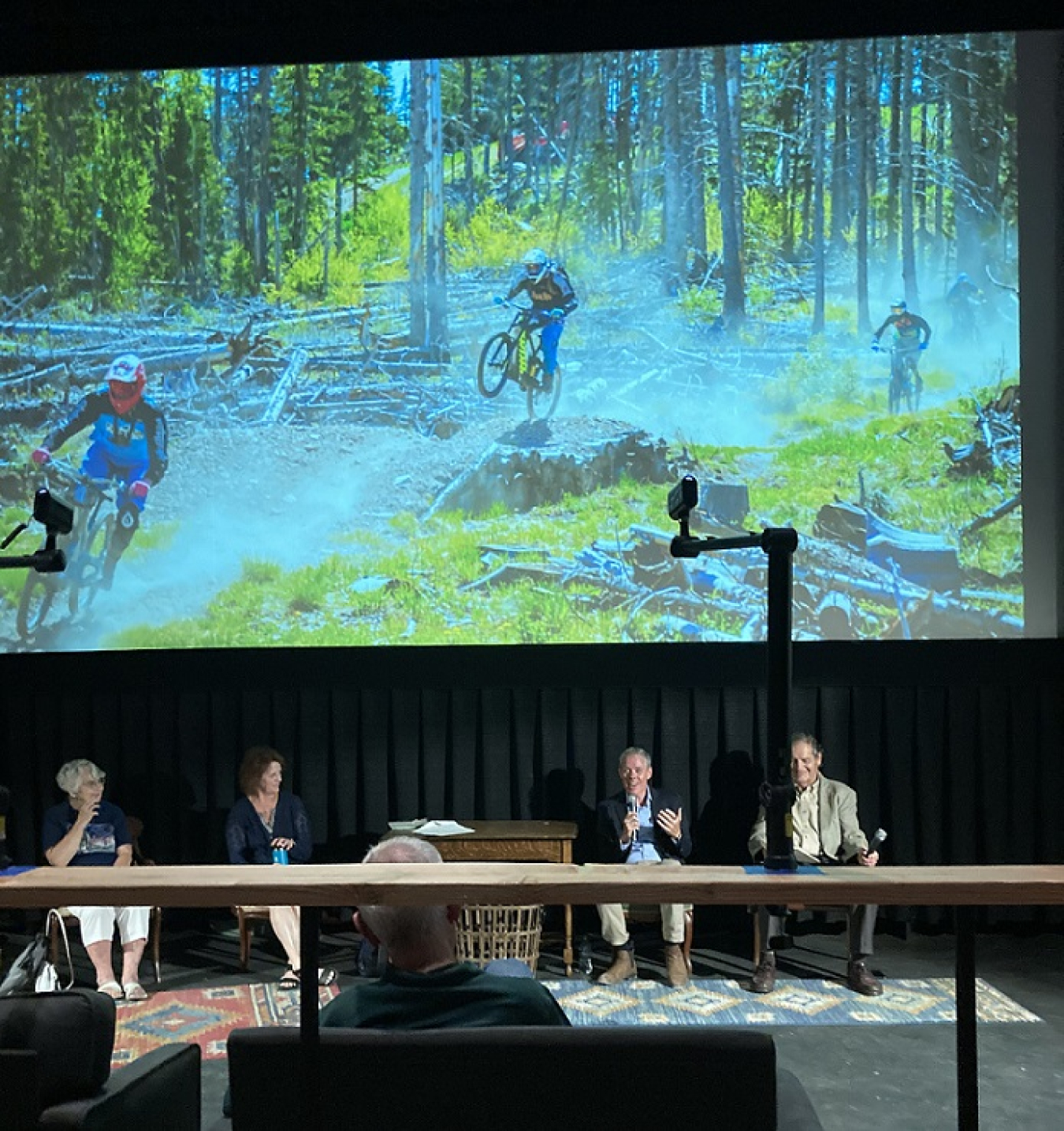 EM Senior Advisor William “Ike” White, second from right, participates on a panel to speak to the history of the Manhattan Project and its legacy during Los Alamos County’s “Oppenheimer Festival 2023.” The panel, “Los Alamos – History, Present and Future,” highlighted visuals of important places in Los Alamos. Shown on the screen is a popular mountain bike trail at Pajarito Ski Mountain. Created in 1957, the ski area originated in 1943 from a group of scientists and soldiers working in Los Alamos during the