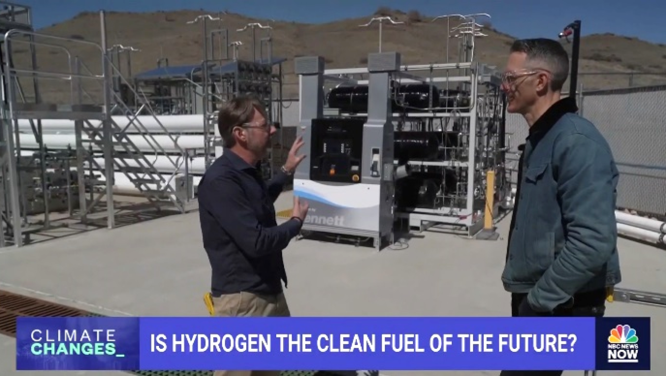 Screenshot from the video, Is Hydrogen the Clean Fuel of the Future?, shows two men talking while standing outdoors next to hydrogen fueling equipment.