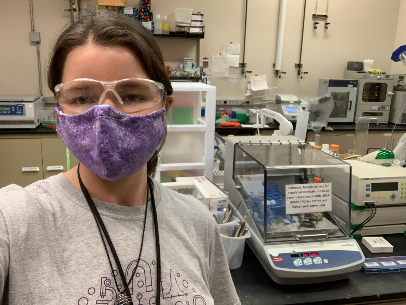 Eva Ottum, wearing safety glasses and a mask, takes a selfie in a lab.