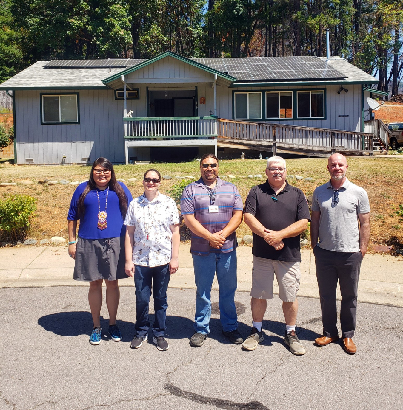 People pose in front of a house with solar panels on the roof.