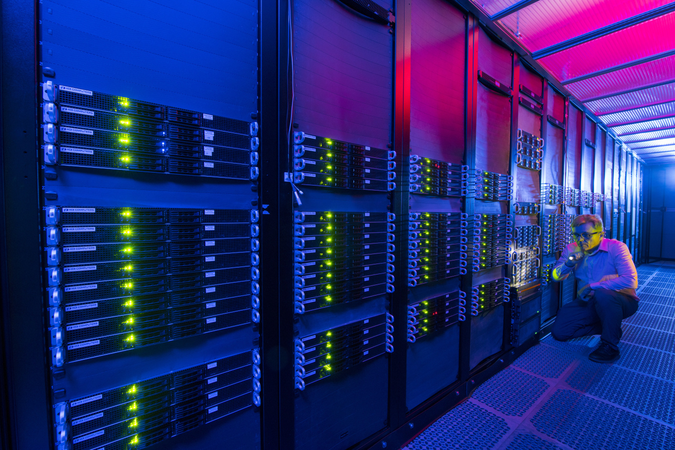 Man kneeling beside illuminated computer servers