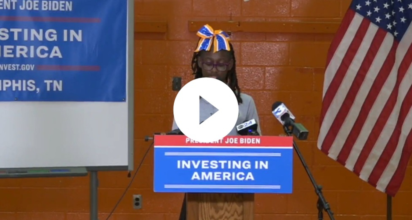 A young woman speaks behind a podium with an "Investing in America" sign on it.
