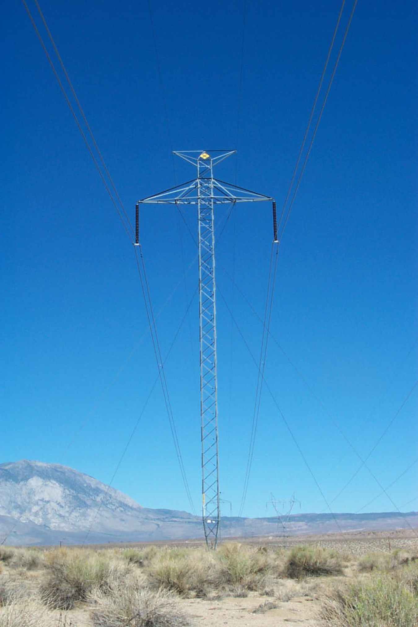 A DC transmission line crosses Highway 365 with sagebrush in the background.