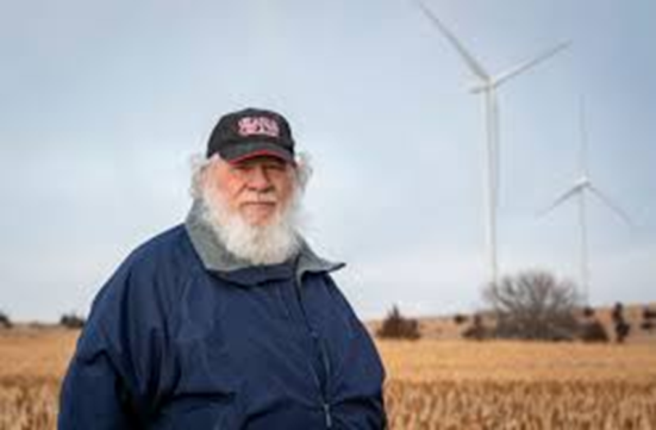 Farmer standing in a grassy area, next to two turbines.