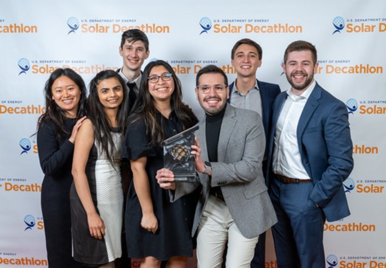 People stand with an award in front of a Solar Decathlon background