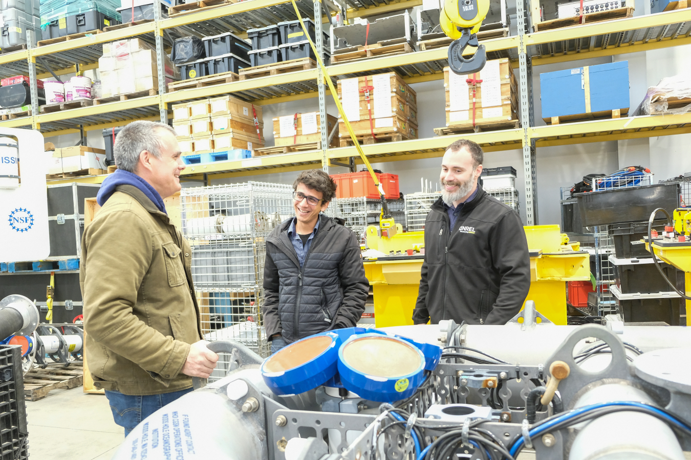 Three people standing in a warehouse next to an inflatable device with metal components and wires in the center