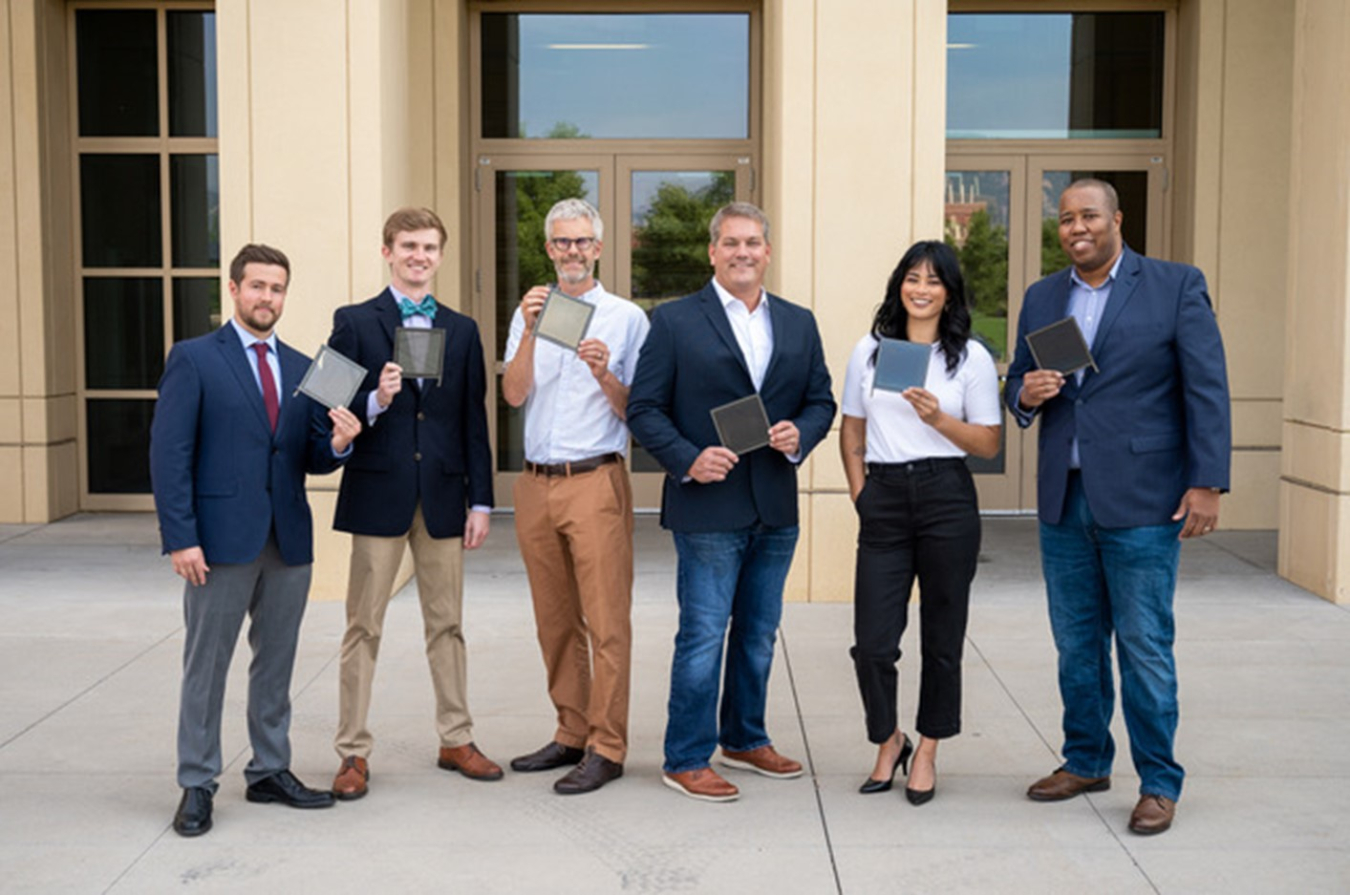 A group of six people in business attire standing outside the entrance of a commercial building, facing the camera.