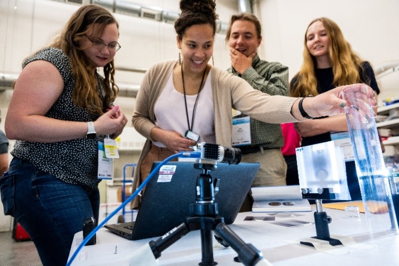 Four young people look at technology examples on a table.