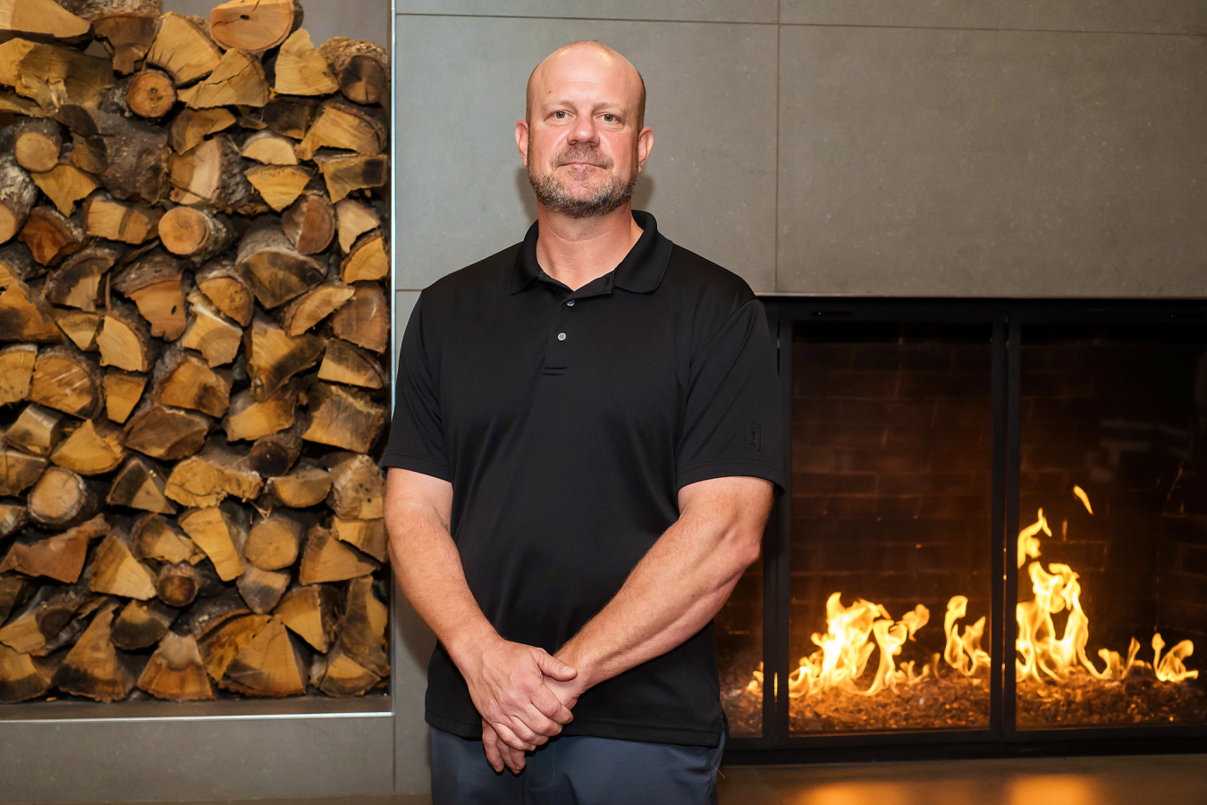 One man poses and smiles for the camera in front of an indoor fireplace.