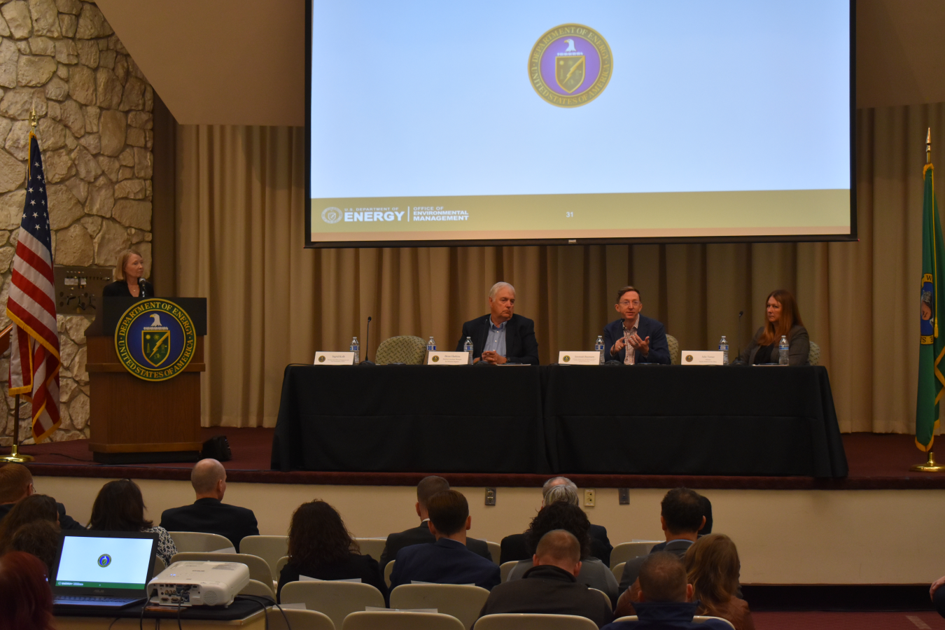Panel of three at table with one speaker at podium taken from back of audience