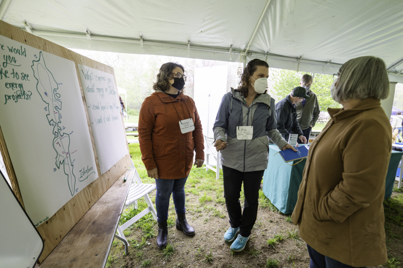 Several people wearing nametags and face masks converse under an outdoor tent.