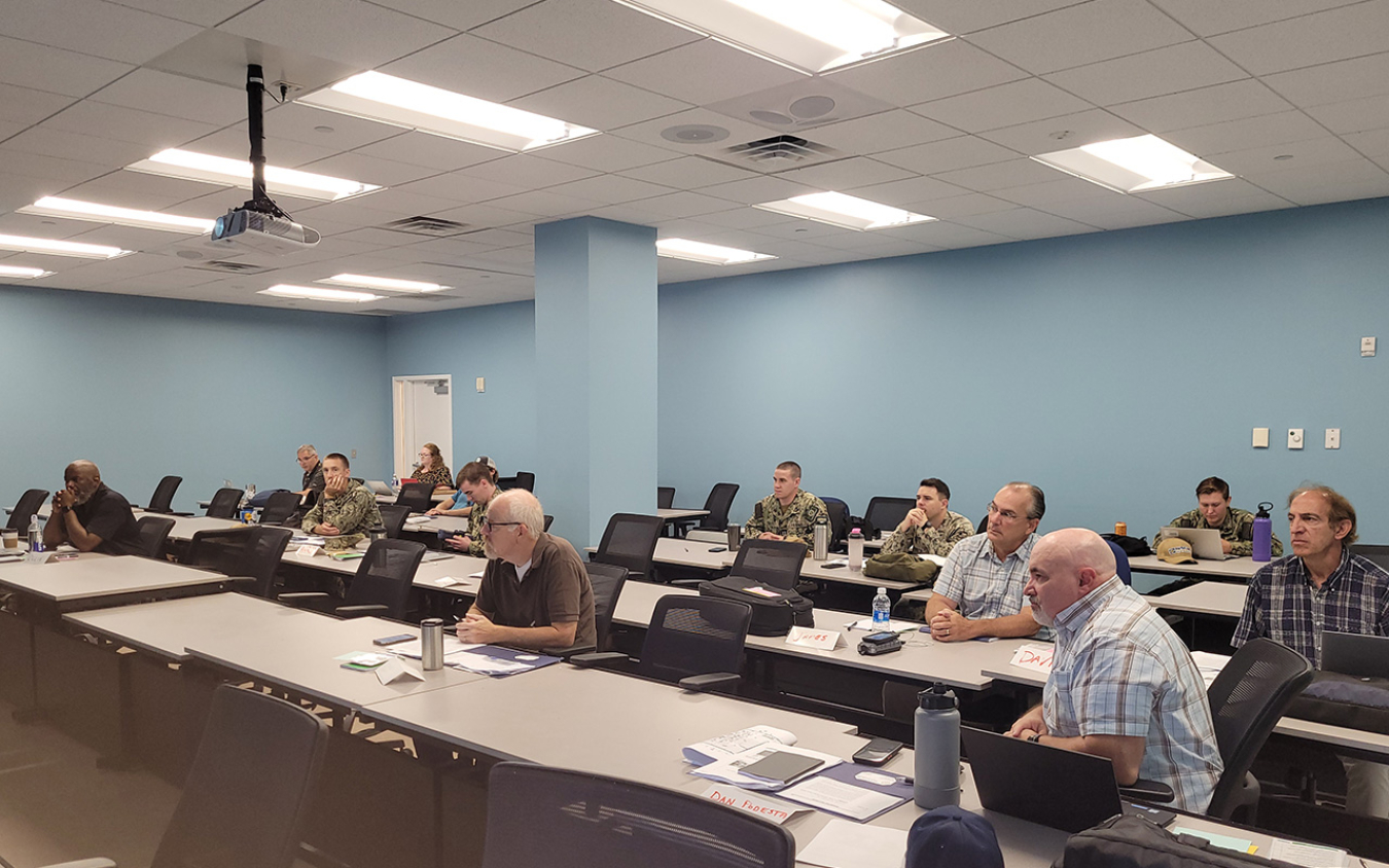 A group of people sitting in a meeting room listening to a speaker who is off screen.